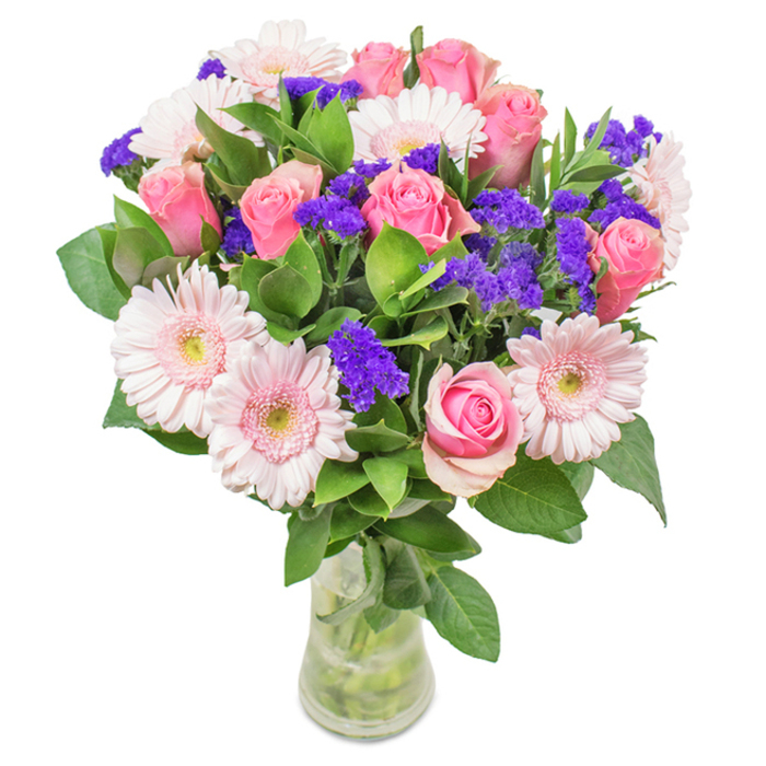 Elegantly arranged in a tall, clear glass vase and set against a crisp white background, this bouquet embodies the natural charm of Charlton. Around seven to nine pink roses compose the heart of the display, each bloom a study in classic spiraling grace, petals in soft to medium pink tones just beginning to open. These are surrounded by five to seven delicate pink gerbera daisies, with their wide, round faces and finely textured pale petals, each ringed by centers shaded almost white. Punctuating this softness, vivid purple statice clusters echo the colour of spring wildflowers near Charlton House, offering striking depth and cheerful contrast. Lush green foliage fans out at the base and between the blooms, infusing the arrangement with the cooling freshness of Maryon Wilson Park. The transparent vase reveals healthy stems and water, reinforcing the bouquet's freshness and sense of natural abundance. Perfect for local birthdays, anniversaries, or as an uplifting accent in a home or office, this bouquet from Charlton Flowers is a heartfelt message of celebration, affection, and enduring vitality.